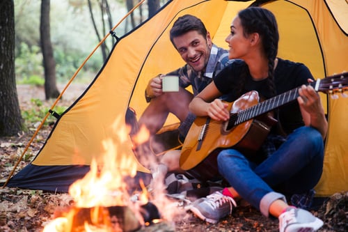 Portrait of a young couple sitting with guitar near bonfire in the forest Portrait of a young couple sitting with guitar near bonfire in the forest