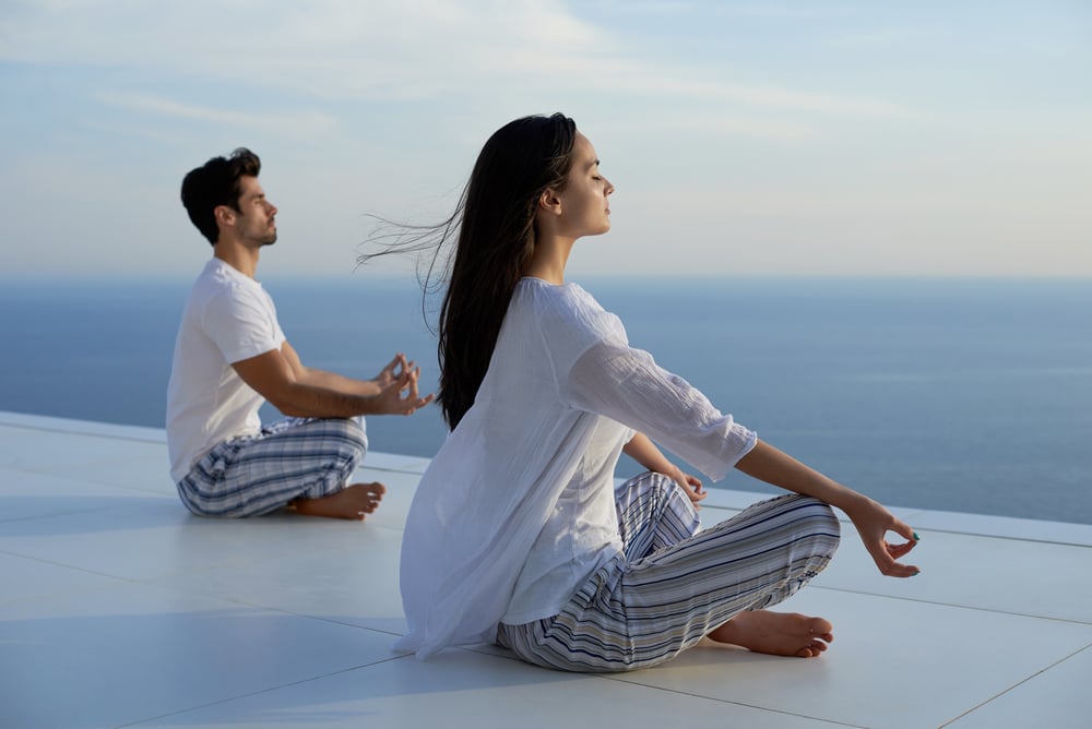 young couple practicing yoga at sunset in modern home terace with ocean and sunset in background young couple practicing yoga at sunset in modern home terace with ocean and sunset in background